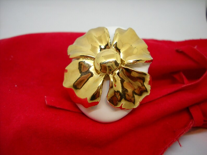 May include: A white ceramic flower with gold accents. The flower is shaped like a bow and has a center with a raised, round, gold detail.