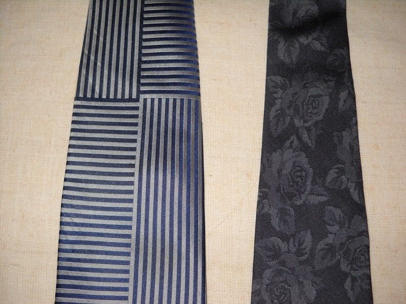 May include: Two neckties, one with a striped pattern in shades of blue and grey, and the other with a black floral pattern.