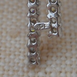 Pode incluir: Close-up de uma pulseira de prata com uma fila de pequenas pedras transparentes. A pulseira tem um fecho com a inscri&ccedil;&atilde;o "12K" nele.