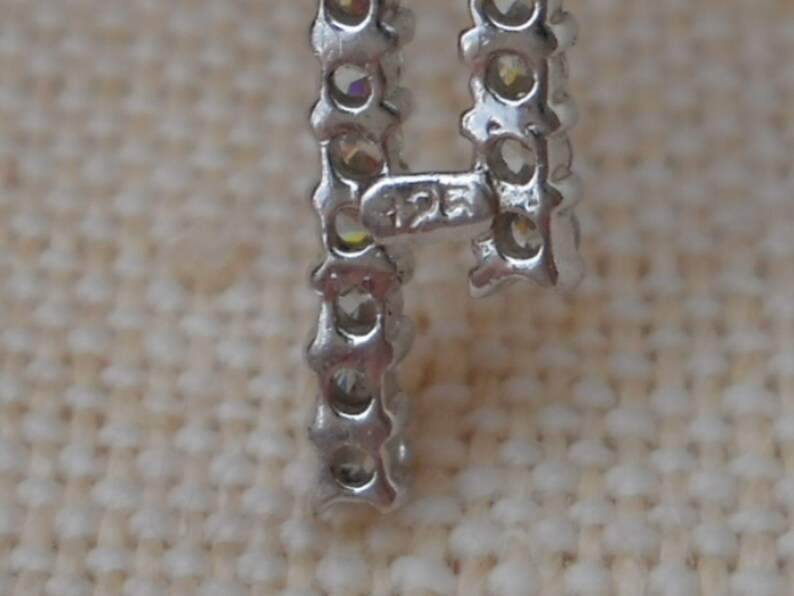 Pode incluir: Close-up de uma pulseira de prata com uma fila de pequenas pedras transparentes. A pulseira tem um fecho com a inscri&ccedil;&atilde;o "12K" nele.