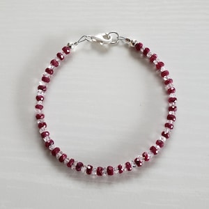 May include: A delicate bracelet made with alternating clear and red faceted beads. The bracelet has a silver clasp.