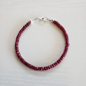 May include: A red gemstone bracelet with a silver clasp. The bracelet is made of small, faceted beads.