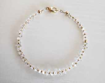 May include: A delicate gold chain bracelet with clear crystal beads. The bracelet has a lobster clasp closure.