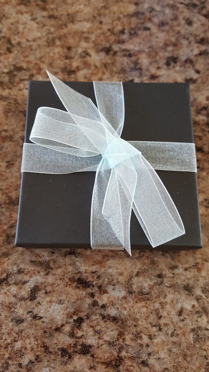 K&ouml;nnte beinhalten: Eine schwarze Geschenkbox mit einem wei&szlig;en durchsichtigen Band, das zu einer Schleife gebunden ist.