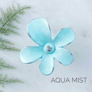 May include: A light blue flower-shaped metal knob with a distressed finish. The knob is labeled "AQUA MIST".