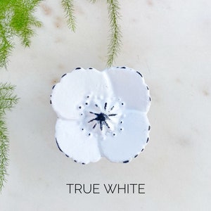 May include: White ceramic flower-shaped knob with black detailing. The knob is a simple, elegant design that would look great on any cabinet or drawer.