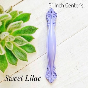 May include: A 3 inch center, lilac colored cabinet pull with a decorative, ornate design.  Sweet Lilac.