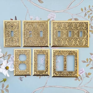 K&ouml;nnte beinhalten: Eine Sammlung verzierter, goldfarbener Lichtschalterabdeckungen und Steckdosenplatten. Die Platten weisen aufwendige Blumen- und Scrollarbeiten auf. Die Kollektion umfasst Einzel-, Doppel- und Dreifachschalterplatten sowie Steckdosenabdeckungen, alle im Vintage-Stil.