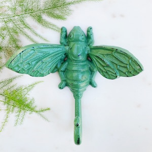 May include: A green cast iron bee hook with a hook at the bottom. The bee has wings and a body with a textured surface.