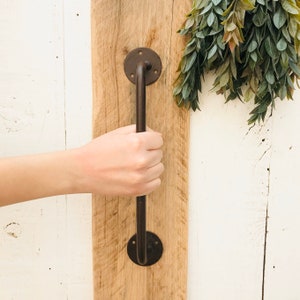 May include: A black metal door handle with a rounded design and two circular plates. The handle is mounted on a wooden surface.