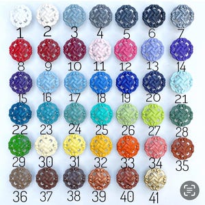 K&ouml;nnte beinhalten: Eine Sammlung von 41 dekorativen runden Kn&ouml;pfen in verschiedenen Farben, angeordnet in Reihen. Zu den Farben geh&ouml;ren Wei&szlig;, Grau, Rot, Rosa, Blau, Gr&uuml;n, Gelb, Orange und Braun. Jeder Knopf hat ein gewebtes Design und ist nummeriert.