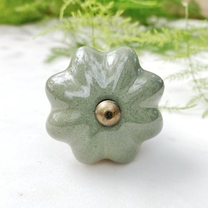 May include: A green ceramic cabinet knob with a gold metal center. The knob is shaped like a flower with five petals.