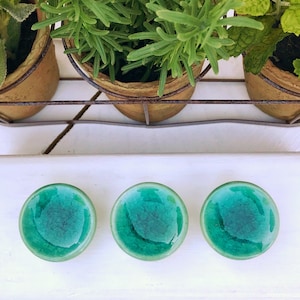 May include: Three teal green glass knobs with a crackled finish. The knobs are round and have a smooth surface.