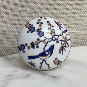 May include: White ceramic knob with a blue and gold bird and floral design.