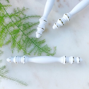 May include: Three white cabinet knobs with gold accents. The knobs have a decorative, ornate design.
