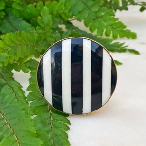 May include: A round, black and white striped cabinet knob with a gold rim.