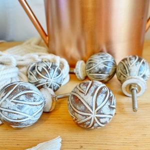 May include: Five white and brown wooden knobs with a carved design. The knobs have a distressed look and are perfect for adding a touch of rustic charm to any home decor project.