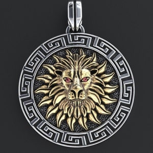 May include: A silver and gold pendant featuring a lion's head with red eyes, surrounded by a black and silver Greek key design.