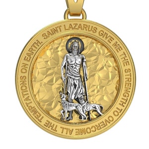 May include: A gold-colored pendant with a detailed depiction of Saint Lazarus, holding a staff and accompanied by a dog. The pendant has a textured background and an outer ring with the inscription "SAINT LAZARUS GIVE ME THE STRENGTH TO OVERCOME ALL THE TEMPTATIONS ON EARTH."