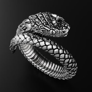 Może przedstawiać: Srebrny pierścionek w kształcie zwiniętego węża z detalicznym głową i łuskami.