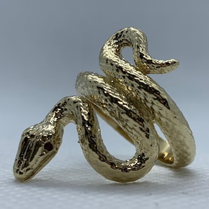 May include: A gold-colored snake ring with a textured surface. The snake's head is detailed with a small red stone for the eye. The ring coils around the finger, creating a unique and eye-catching design.