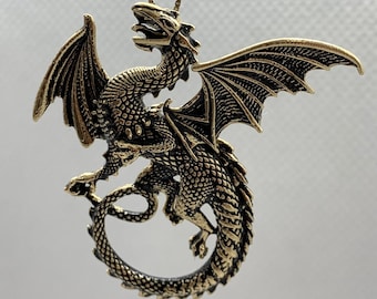 May include: A gold-toned dragon pendant necklace with intricate details. The dragon is curled up with its wings spread out. The pendant is attached to a chain.