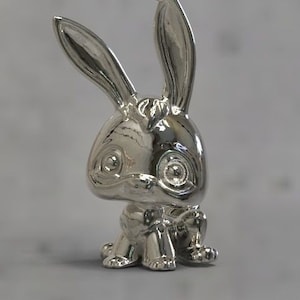 May include: A silver charm necklace pendant featuring a rabbit with large eyes and a shiny finish.