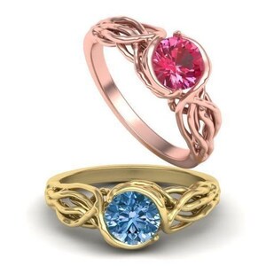 May include: Two gold rings with intricate designs. The ring on the left has a blue gemstone, while the ring on the right has a pink gemstone.