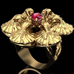 Puede incluir: Un anillo de oro con una piedra preciosa roja en el centro. El anillo está diseñado con cinco figuras en un círculo, cada una con una falda fluida.