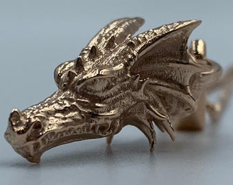 May include: A gold-toned dragon head pendant necklace. The dragon's head is detailed with scales and has a textured finish.
