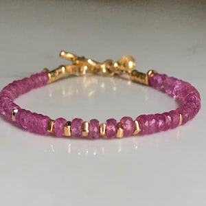 Puede incluir: Un delicado brazalete de oro con cuentas de piedras preciosas rosas. El brazalete tiene un cierre de palanca.