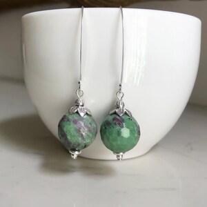 May include: A pair of silver dangle earrings with green and purple gemstone beads.