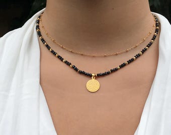 May include: A gold chain necklace with a black beaded chain and a gold coin pendant. The coin pendant has a detailed design.