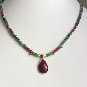 May include: A delicate necklace with a teardrop-shaped ruby pendant. The necklace is made with green and pink beads.