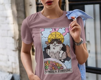 May include: A mauve t-shirt with a graphic of a cat sitting in a bowl of cereal. The graphic is a parody of the Wheel of Fortune tarot card. The text on the card reads "Wheel of Fortune".
