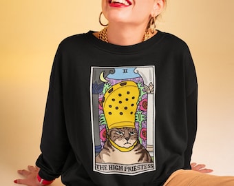 May include: Black sweatshirt with a graphic of a cat wearing a yellow Croc shoe as a crown. The graphic is a parody of the High Priestess tarot card. The text "THE HIGH PRIESTESS" is printed below the graphic.