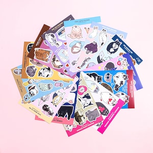May include: A collection of 16 sticker sheets featuring various illustrations of cats in different poses and situations. The sticker sheets are colourful and have a variety of backgrounds, including pink, blue, yellow, and green. The sticker sheets are arranged in a fan shape on a pink background.