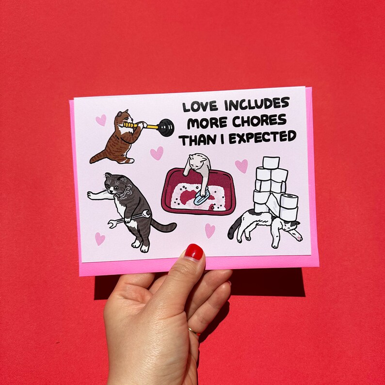 May include: A pink card with a humorous illustration of cats doing chores. The text reads "Love includes more chores than I expected."