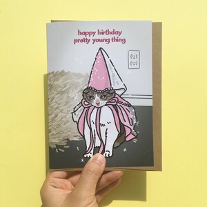 May include: A birthday card featuring a cartoon cat wearing a pink princess crown and cape. The card reads "happy birthday pretty young thing".