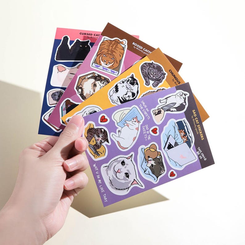 May include: A set of six colourful sticker sheets featuring various cat illustrations. The stickers include cats in boxes, sad cats, cats with funny expressions, and cats with text like "Why u do me like that" and "This could be us".