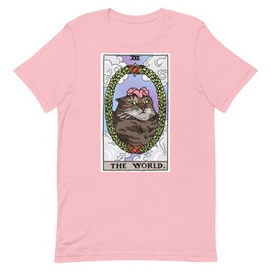 Pu&ograve; includere: Una t-shirt rosa con una grafica di un gatto che indossa una corona di fiori. La grafica &egrave; una carta dei tarocchi con il testo "XXI THE WORLD."