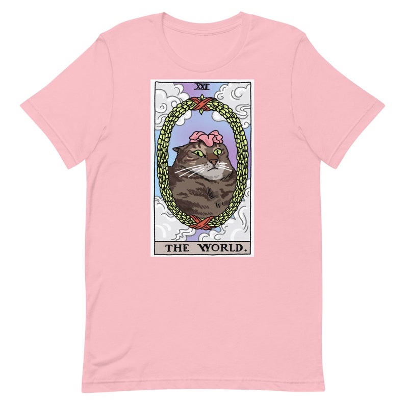Pu&ograve; includere: Una t-shirt rosa con una grafica di un gatto che indossa una corona di fiori. La grafica &egrave; una carta dei tarocchi con il testo "XXI THE WORLD."