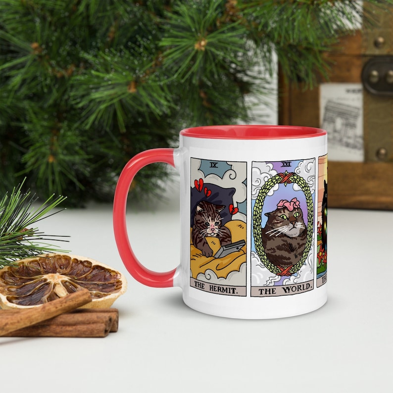 Puede incluir: Taza de cer&aacute;mica blanca con borde rojo. La taza presenta un dise&ntilde;o de cuatro cartas de tarot con gatos representados como los personajes. Las cartas son "El Ermita&ntilde;o", "El Mundo", "La Torre" y "La Estrella".