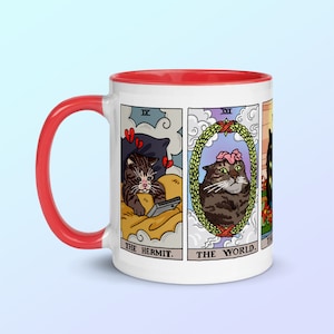 Puede incluir: Taza de cer&aacute;mica blanca con borde rojo. La taza presenta un dise&ntilde;o de cuatro cartas de tarot con gatos. Las cartas son "El Ermita&ntilde;o", "El Mundo", "La Torre" y "Los Enamorados".