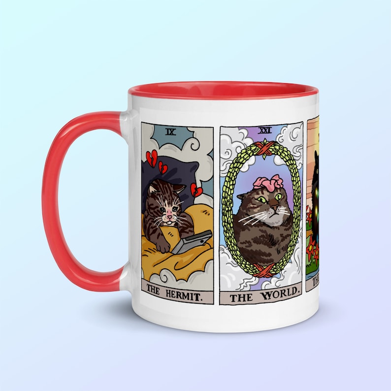 Puede incluir: Taza de cer&aacute;mica blanca con borde rojo. La taza presenta un dise&ntilde;o de cuatro cartas de tarot con gatos. Las cartas son "El Ermita&ntilde;o", "El Mundo", "La Torre" y "Los Enamorados".