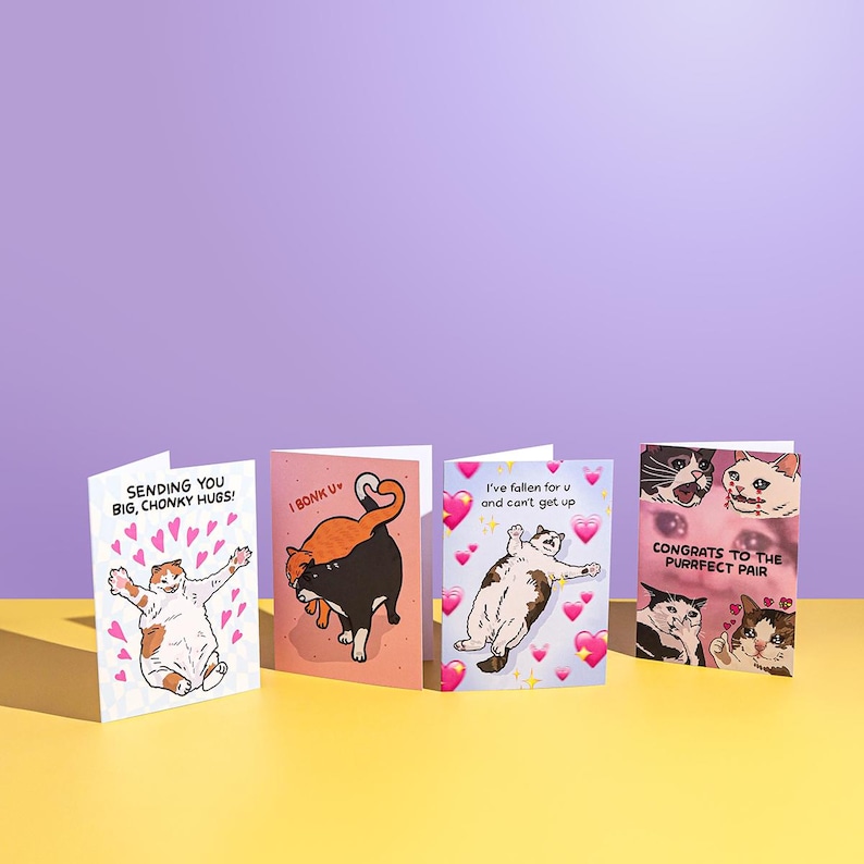 Puede incluir: Cuatro tarjetas de felicitaci&oacute;n con ilustraciones de gatos. Las tarjetas presentan frases como "Sending you big, chonky hugs!" y "Congrats to the purrfect pair." Cada tarjeta tiene un dise&ntilde;o &uacute;nico con corazones y gatos de dibujos animados.