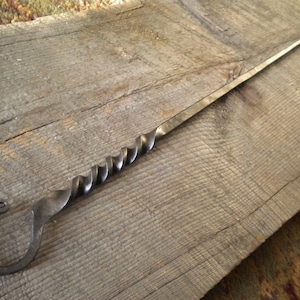 May include: A twisted metal fireplace poker with a loop handle. The poker is made of dark metal and has a rustic look.