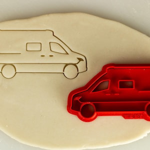 Puede incluir: Un cortador de galletas de plástico rojo con forma de furgoneta. El cortador está sobre una superficie blanca con un contorno blanco de la furgoneta.