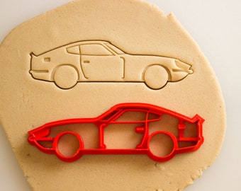 May include: A red plastic cookie cutter in the shape of a vintage sports car. The cutter is on top of a piece of cookie dough, with an impression of the cutter in the dough.