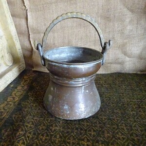 May include: A vintage copper bucket with a brass handle. The bucket has a worn, aged patina and is slightly dented.